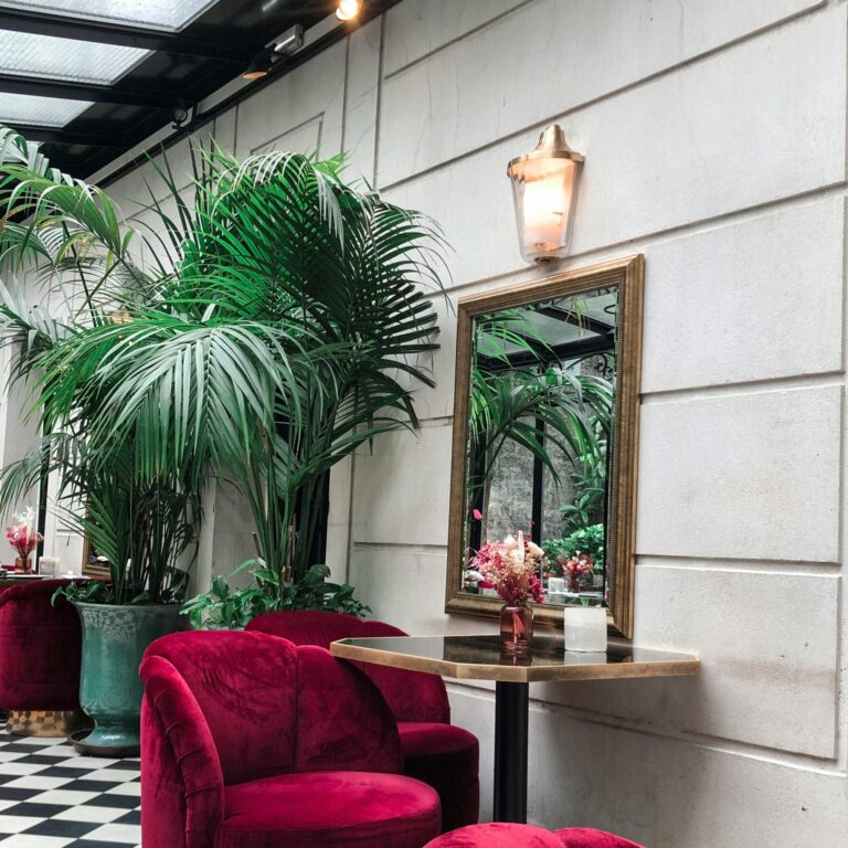 Stylish Parisian interior featuring red velvet chairs, tropical plants, and a classic mirror.