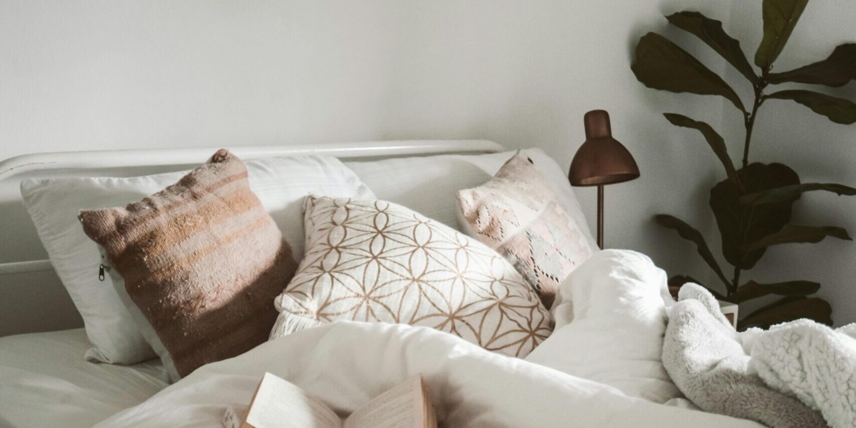 Warm and inviting bedroom setup with decorative pillows, plants, and an open book for a cozy ambiance.
