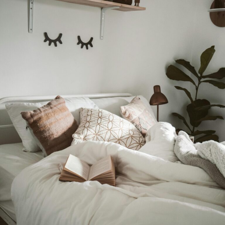 Warm and inviting bedroom setup with decorative pillows, plants, and an open book for a cozy ambiance.