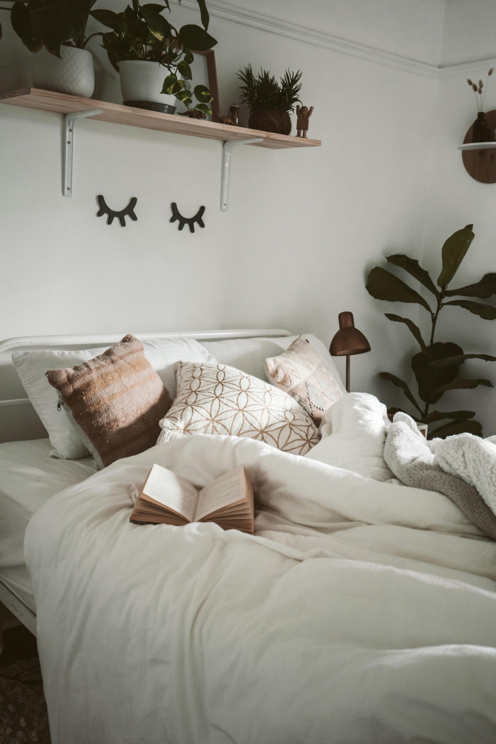 Warm and inviting bedroom setup with decorative pillows, plants, and an open book for a cozy ambiance.